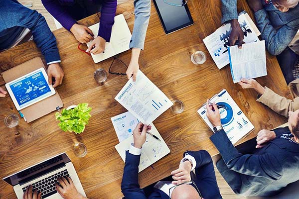 Overhead view of business team meeting at wooden table with laptops, charts and documents