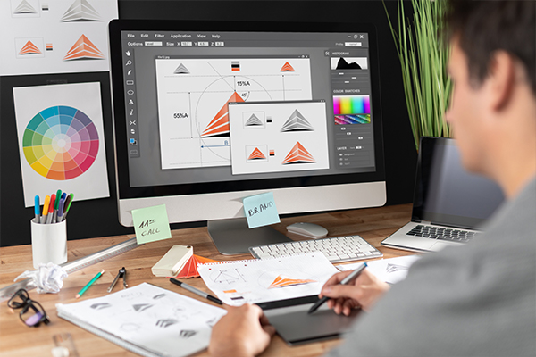 Graphic designer working on triangle logo in design software with color wheel and sketches on desk